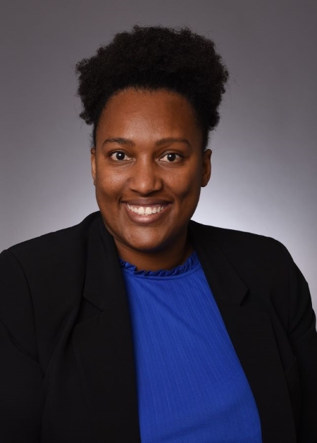 Smiling woman with black hair wearing a black jacket over a royal blue shirt.